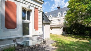 A building with a glass table and chairs outside, a stone wall, and a tree in the background. - The royal escape (Saint-Benoît-la-Forêt)