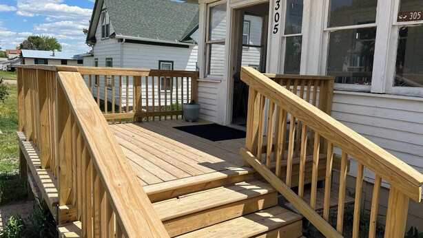 Eine Holzterrasse mit einer Treppe, die zu einem weißen Gebäude mit der Nummer 305 führt.