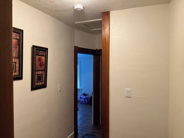 A hallway with a wooden door leading to a room. There are framed pictures on the wall.