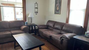 A living room with two brown leather sofas, a wooden coffee table, a small table with a lamp, and a framed artwork on the wall.