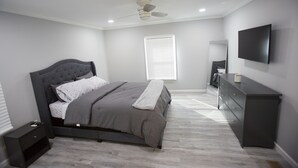 Une chambre à coucher comprenant un lit, une commode, un téléviseur et un ventilateur de plafond.