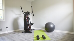 Une salle de sport à domicile équipée d’un appareil elliptique, d’un grand ballon d’exercice et d’haltères posés sur un tapis vert.