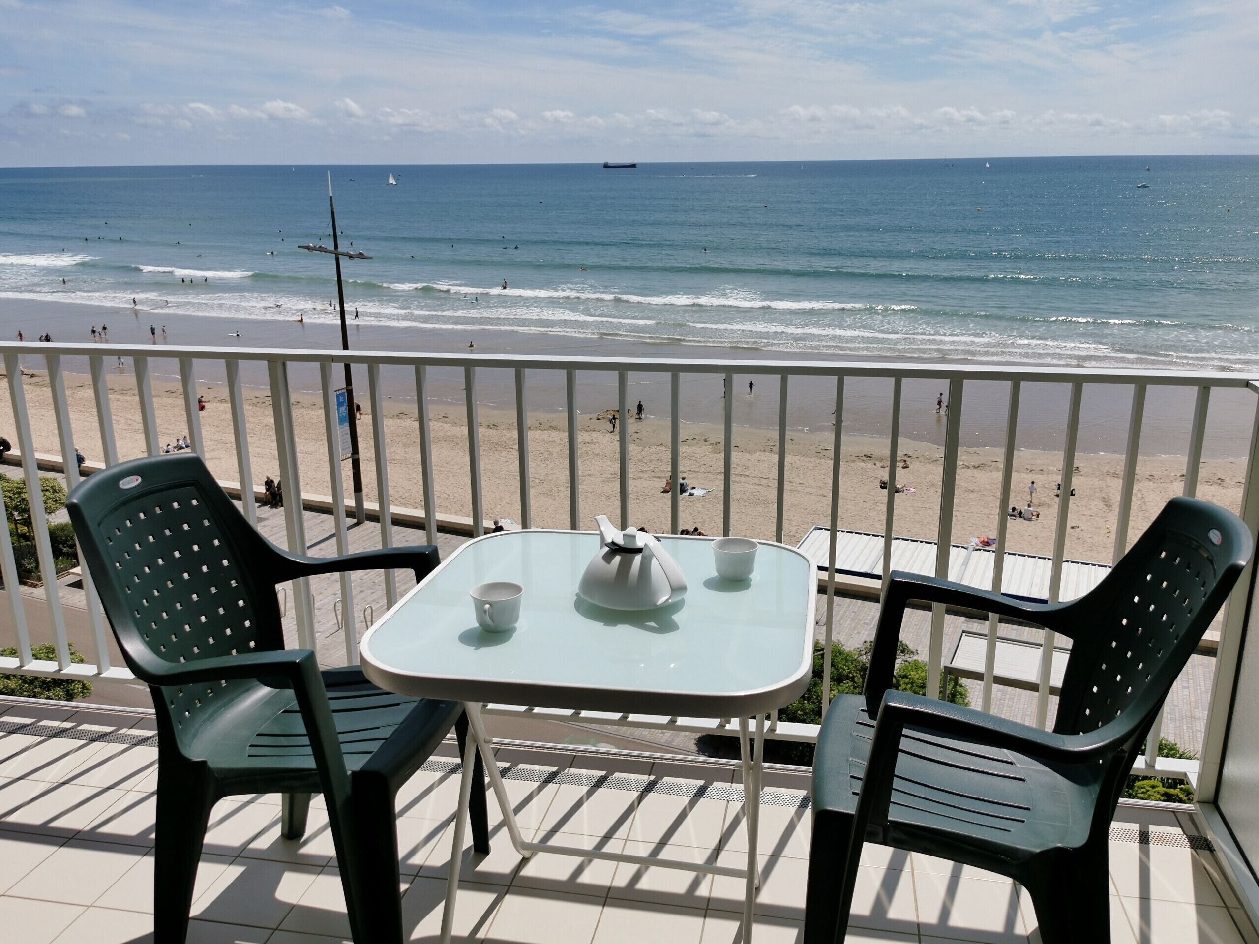 Een balkon met een tafel en stoelen, uitkijkend op een strand.