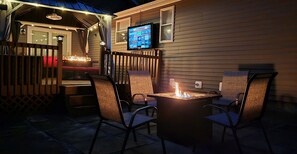 An outdoor patio with a fire pit, seating, and a TV mounted on the wall.