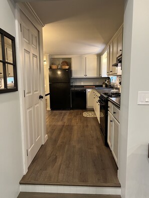 A narrow kitchen with white cabinets, a black refrigerator, and a wooden floor.