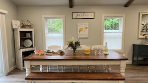 A dining area with a wooden table set for a meal, two windows, and a 'gather' sign above the table. - The Silliman House - New renovation, Farmhouse Chic, close to baseball parks (maryland)