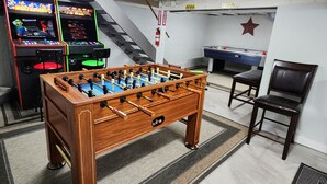 Une pièce équipée d’un baby-foot en bois, de deux bornes d’arcade, d’une table de billard et d’un extincteur.