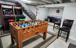 Een kamer met een houten tafelvoetbaltafel, twee speelautomaten, een pooltafel en een brandblusser.