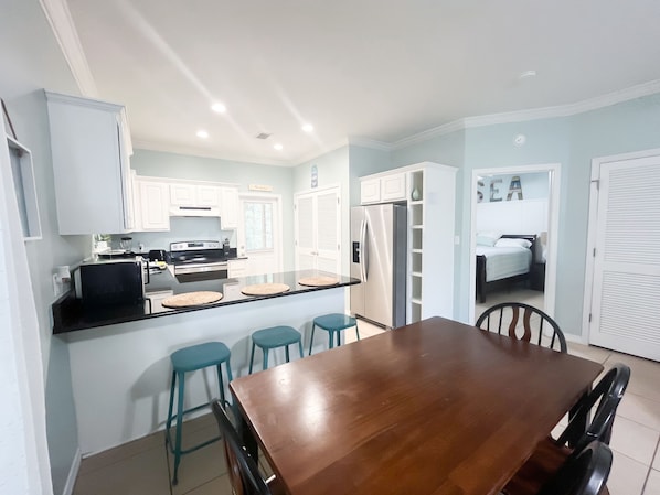 A compact kitchen with white cabinets, a black stove, and a refrigerator. There is a wooden dining table with four chairs. - Poolside Escape in Orange Beach Near Beaches, Golf, The Wharf & Sportsplex (Orange Beach)
