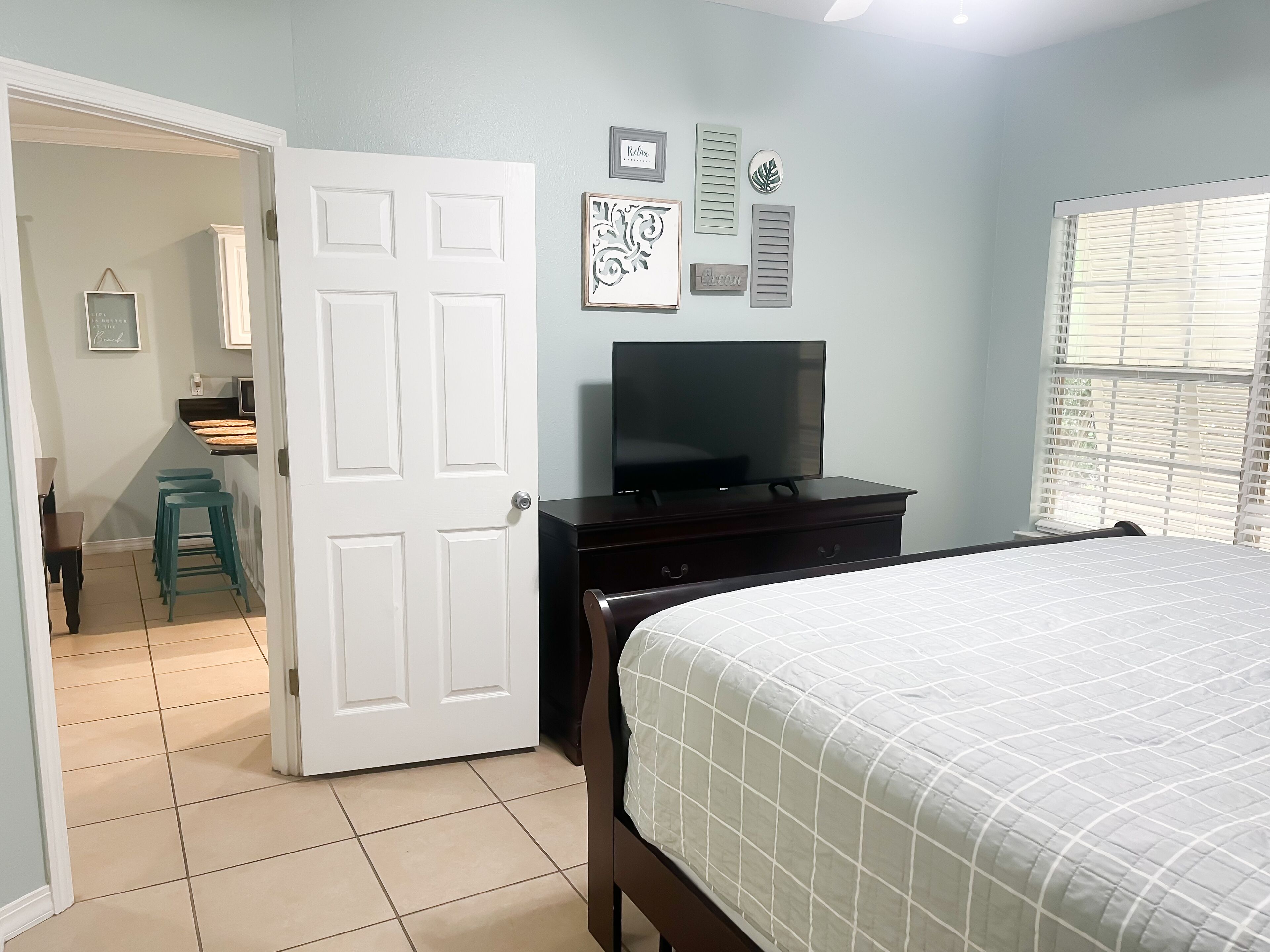 A bedroom with a bed, a dresser, a TV, and a window with blinds.