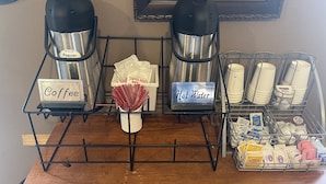 A coffee station with two kettles, labeled 'Coffee' and 'Hot Water', and a basket of straws. - Baranof Lodge (Sitka)