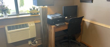 Un bureau à domicile équipé d’un bureau, d’un ordinateur, d’une imprimante et d’une grande fenêtre donnant sur un paysage verdoyant.