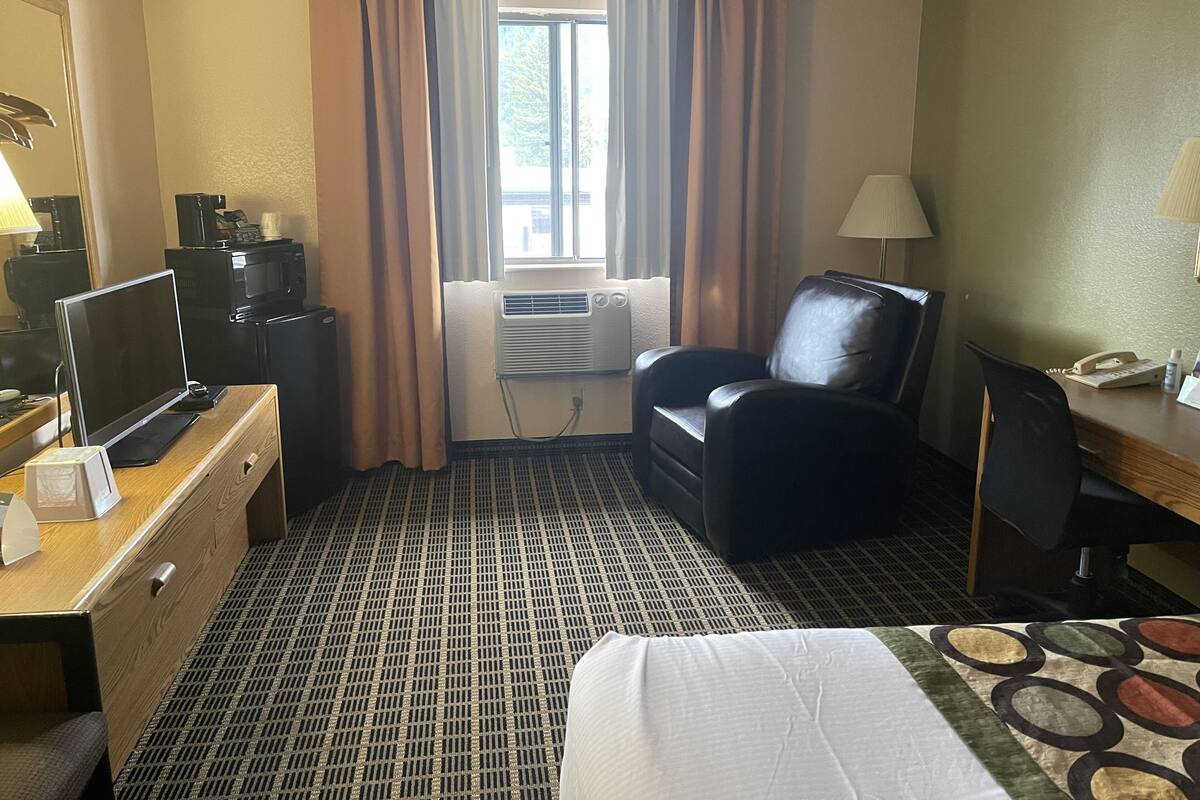 Une chambre d’hôtel comprenant un lit, un bureau, une chaise, une télévision, un climatiseur et une fenêtre avec des rideaux.