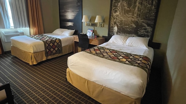 A hotel room with two beds, a desk, a chair, and a large painting on the wall. - Baranof Lodge (Sitka)