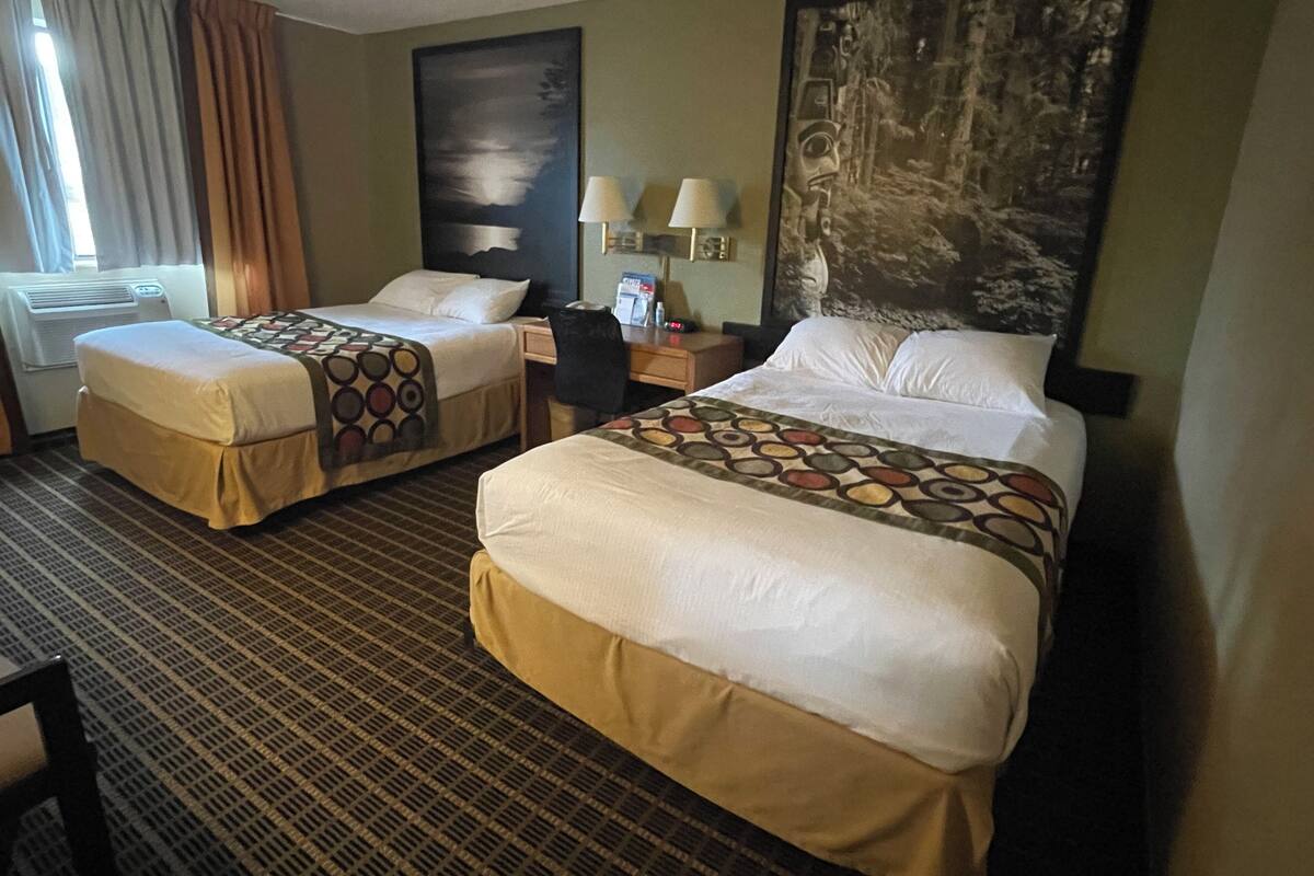 Une chambre d’hôtel avec deux lits, un bureau, une chaise et un grand tableau au mur.