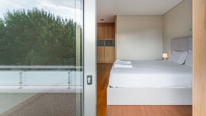 Een moderne slaapkamer met een groot bed, een nachtkastje en uitzicht op bomen door een glazen deur.