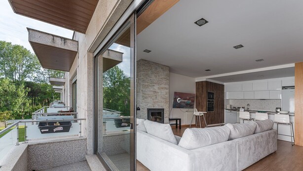 Een moderne woonkamer met een grote glazen deur naar een balkon, een ingebouwde open haard en een keuken met witte kasten en een houten accentmuur.