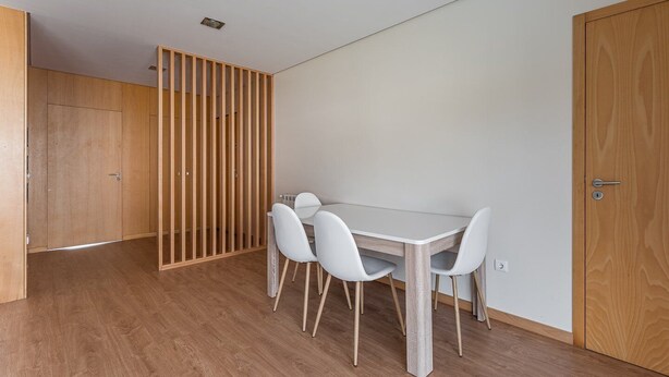 Ein Zimmer mit Holzboden, einem weißen Tisch mit vier Stühlen und einer Holzwand.