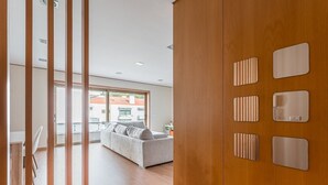 Een modern interieur met een houten garderobe, een witte bank en uitzicht door een glazen deur naar buiten.