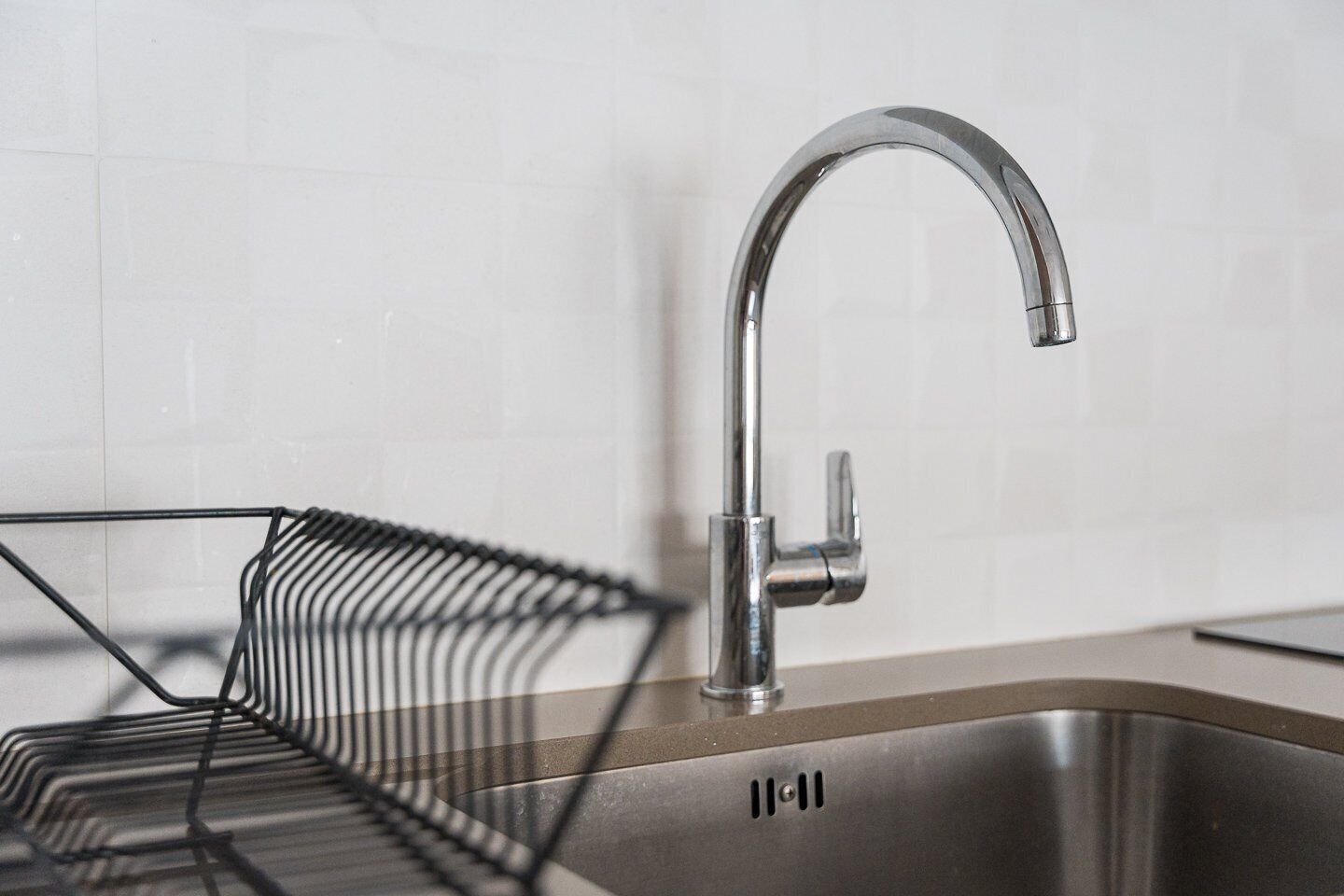 Una cucina moderna con lavello in acciaio inossidabile, portabiancheria metallico e parete di fondo rivestita di piastrelle bianche.