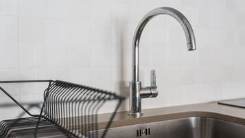 Una cucina moderna con lavello in acciaio inossidabile, portabiancheria metallico e parete di fondo rivestita di piastrelle bianche.
