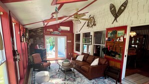 A cozy living room with a brick floor, red walls, and a large window. There is a brown leather sofa, a coffee table, and a rug.