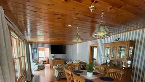 A wooden dining area with a round table and chairs, a chandelier, and a view into another room with a sofa and a television.