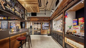 Un moderno interior de cafetería con una zona de bar, taburetes y una exhibición de productos para el desayuno.