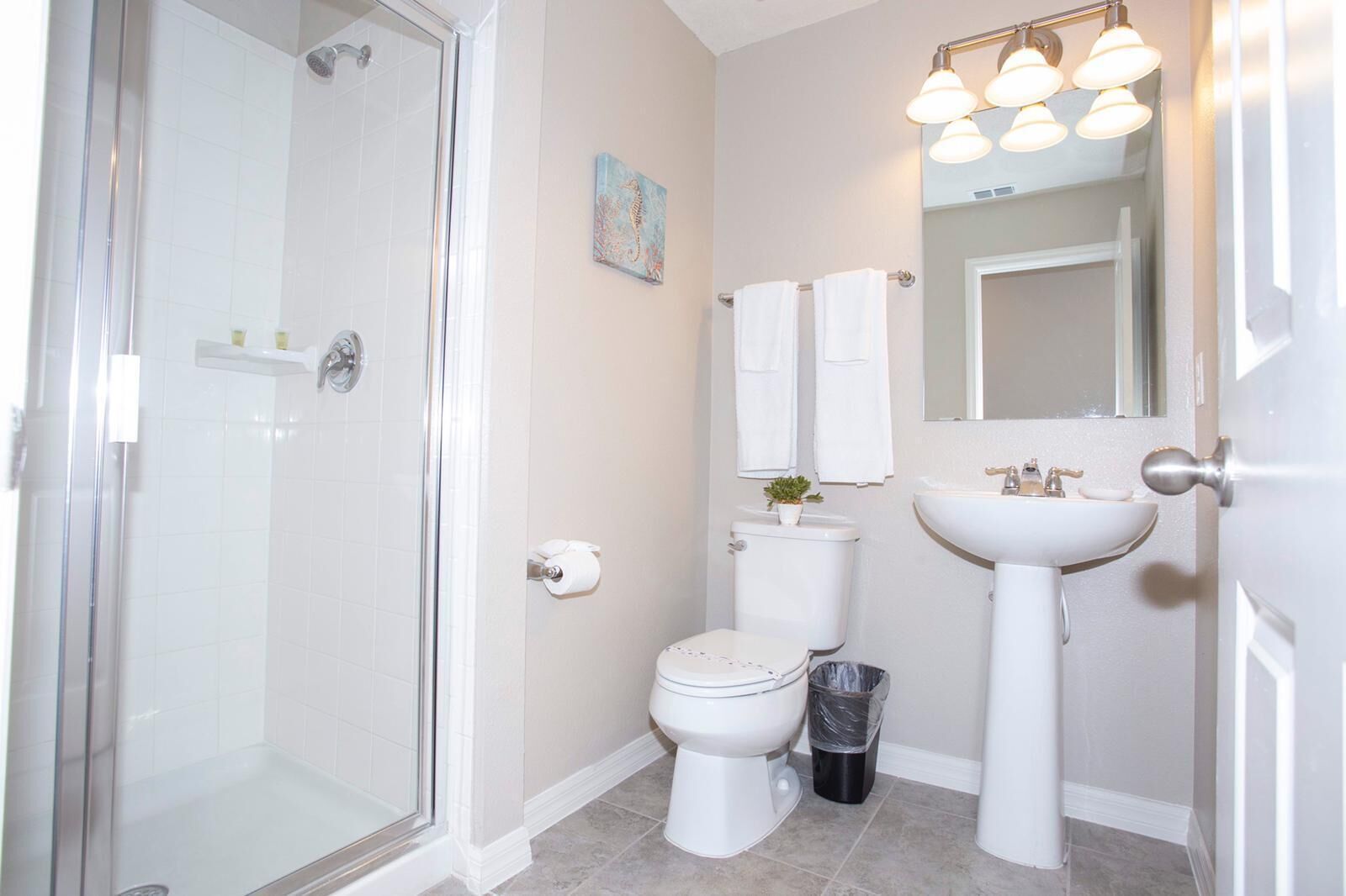 A bathroom with a glass shower enclosure, a toilet, a sink, and a mirror with three lights.