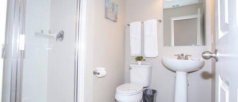 A bathroom with a glass shower enclosure, a toilet, a sink, and a mirror with three lights.