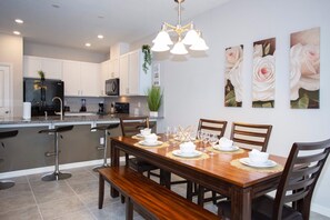 A modern kitchen with white cabinets, a black refrigerator, and a dining area with a wooden table set for four. - 5146 Amazing Townhome 4bd/3.5bth Near Disney Parks (Kissimmee)