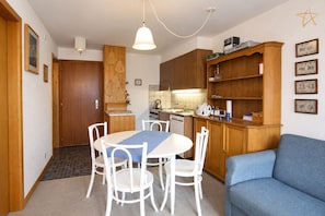 A compact kitchen with a dining area, wooden cabinets, and a blue sofa. - Cosy apartment with south-facing balconyOutside : apartment on the 2nd floor with south-facing balco (St-Luc)