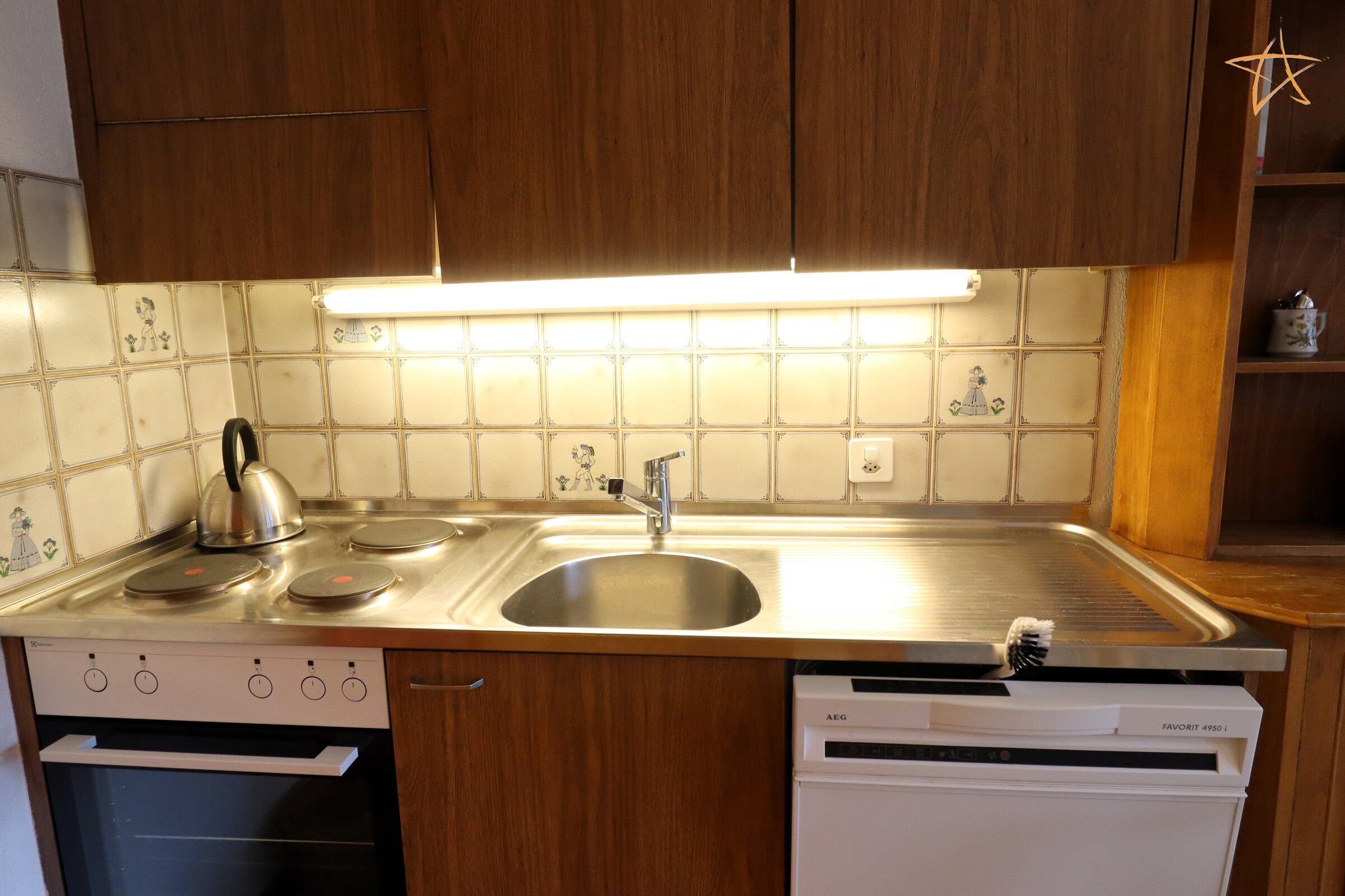 Una cocina con un lavamanos de acero inoxidable, un hervidor y un lavavajillas.