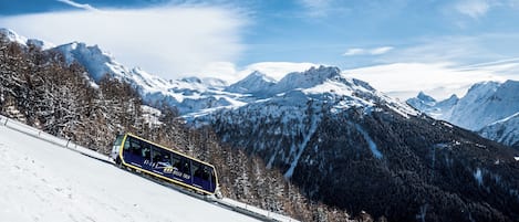 Un train circule sur une voie ferrée de montagne enneigée, avec des montagnes couvertes de neige en arrière-plan.