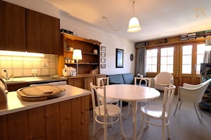 A cozy kitchen with wooden cabinets, a dining table with chairs, and a window with curtains.