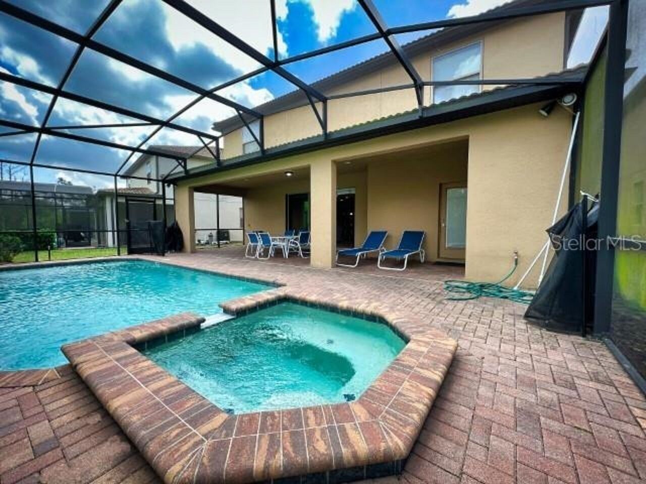 A swimming pool with a glass enclosure, lounge chairs, and a brick patio area.