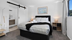 Un dormitorio moderno con cama, mesitas de noche, una ventana con cortinas y un cuadro en la pared.
