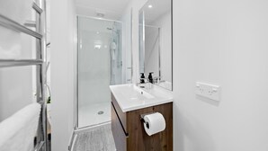 Un baño moderno con cabina de ducha de vidrio, un lavabo blanco y un mueble de tocador de madera.