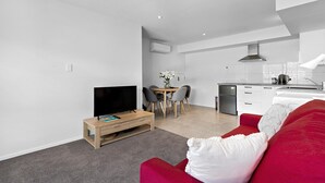 Una sala moderna con un sofá rojo, un televisor sobre un mueble de madera y un comedor con mesa y sillas.