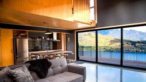 A modern kitchen with a large island, a dining area, and a sofa with a view of a lake and mountains.
