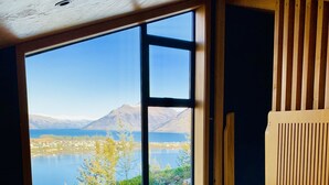 A bedroom with a large window offering a view of a lake and mountains.