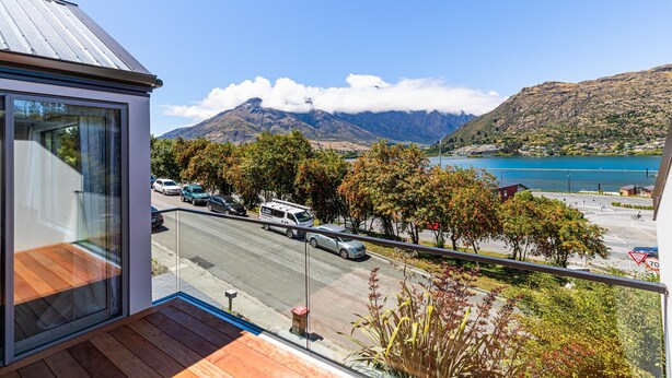 Um edifício moderno com varanda que oferece vista para uma rua, uma montanha e um lago.