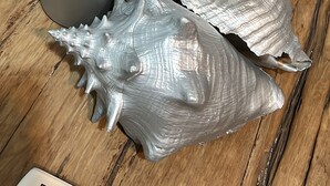 Metallinen maljakko ja kaksi erikoispintaisia esinettä puupinnalla.