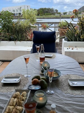 An outdoor dining area with a table set for two, featuring a variety of dishes, drinks, and a candle centerpiece.