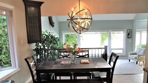 Comedor con una mesa de madera oscura, seis sillas, un jarrón con flores y una moderna lámpara esférica.