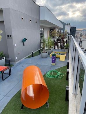 A rooftop terrace with a slide, potted plants, and a yellow play area.