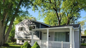 A two-story house with a front porch, surrounded by trees and a well-maintained lawn. - Comfortable 4 Bedroom / 1.5 Bathroom Home (Ypsilanti)
