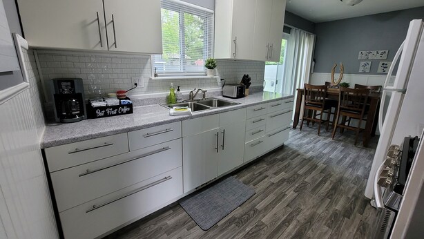 A modern kitchen with white cabinets, a built-in oven, a coffee maker, and a dining area with wooden chairs and a table. - Comfortable 4 Bedroom / 1.5 Bathroom Home (Ypsilanti)