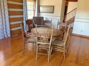 A wooden dining table surrounded by six chairs, a window with curtains, a framed picture on the wall, and a staircase in the background. - Lake house (Old Hickory)