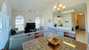A spacious living room with a sofa, a dining table with a bowl, a TV, and a ceiling fan. - Great 1 BDR Condo in the center of Myrtle Beach (Myrtle Beach)